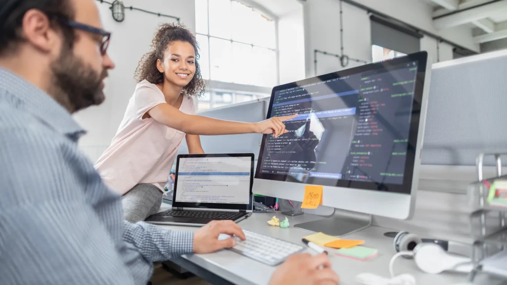Professionals collaborating on custom website development services, writing code and discussing design on large monitors.